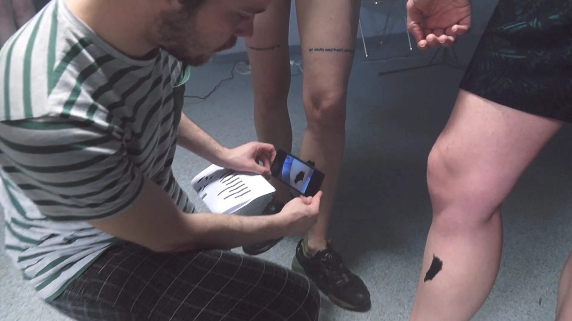 A participant holding a phone near a temporary graphic mark on another person’s leg