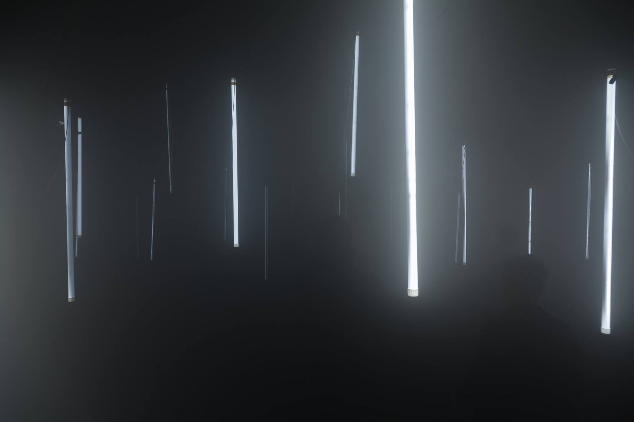 An installation detail: bright vertical light objects and darker suspended objects in haze.