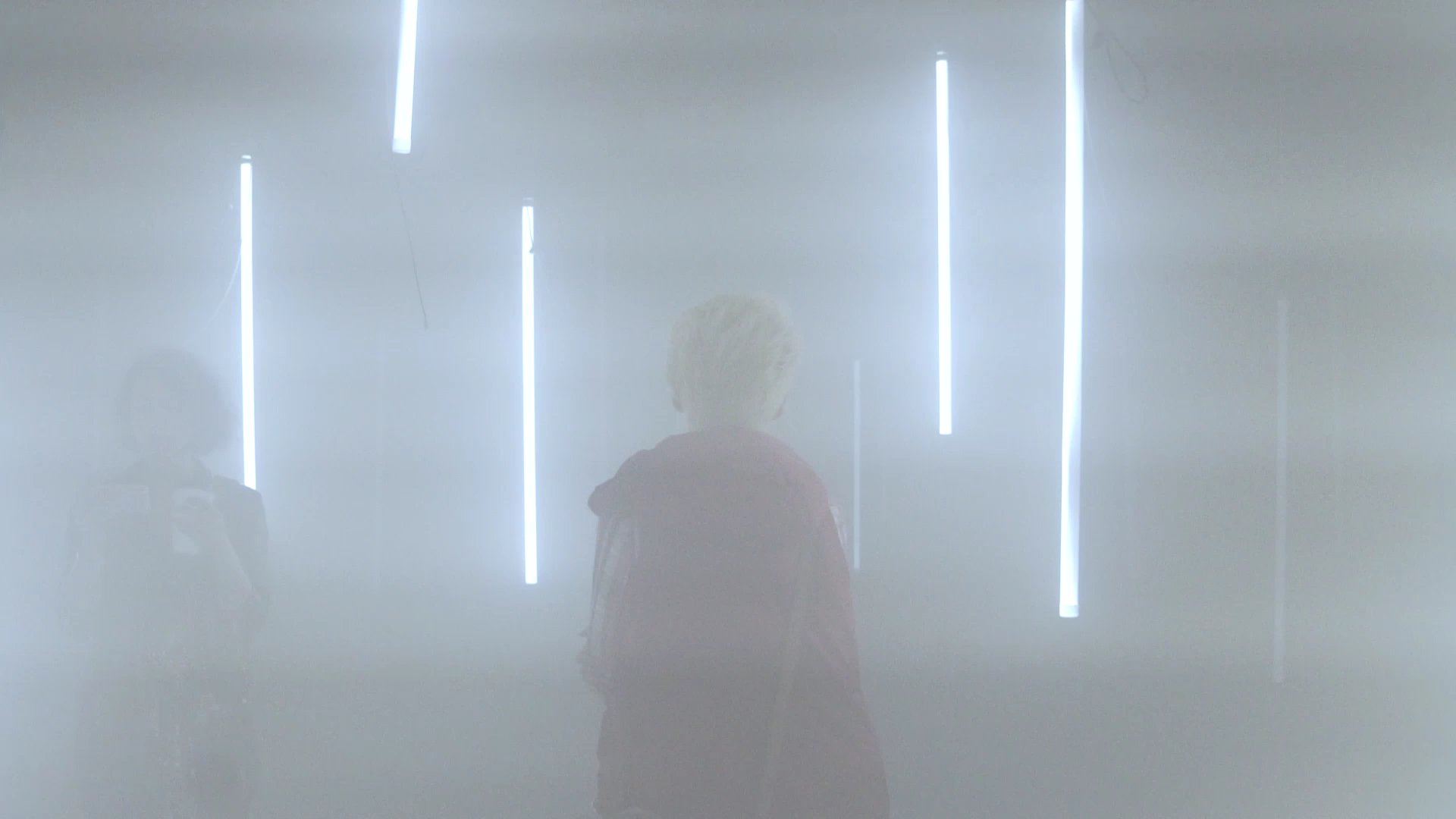 Two visitors among illuminated light objects in a pale haze.